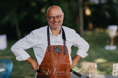 Un chef cuisine sur un barbecue rond dans un jardin aménagé avec des tables et des plantes.