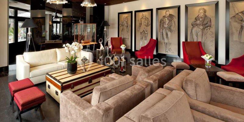 Salon élégant avec canapés beiges, fauteuils rouges, table basse en bois et dessins encadrés sur un mur clair.