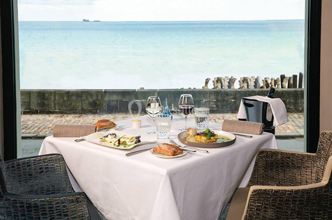 Table dressée pour deux avec vue sur la mer, plats servis, pain, verres de vin et eau, dans un cadre lumineux.