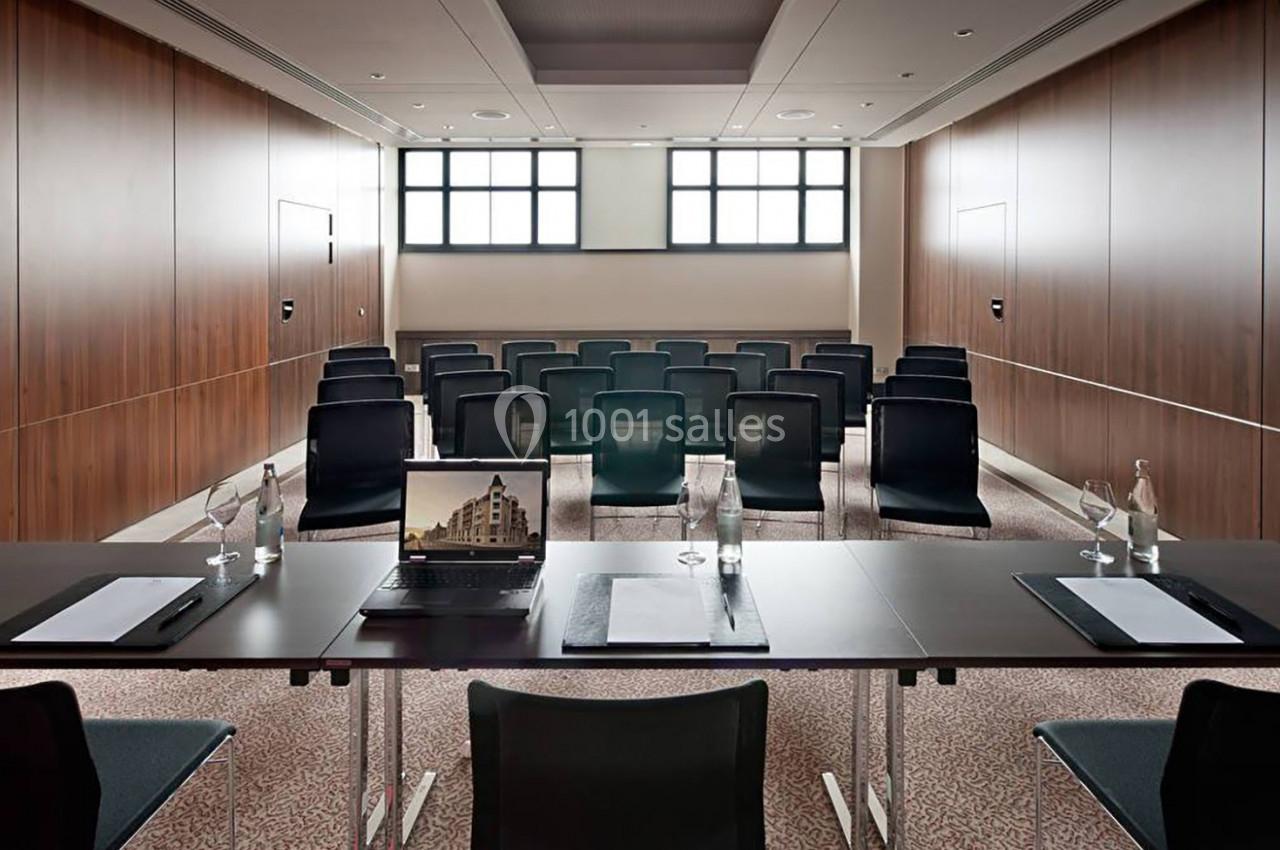 Salle de réunion avec rangées de chaises, table équipée de carnets, stylos, bouteilles d'eau et un ordinateur portable.