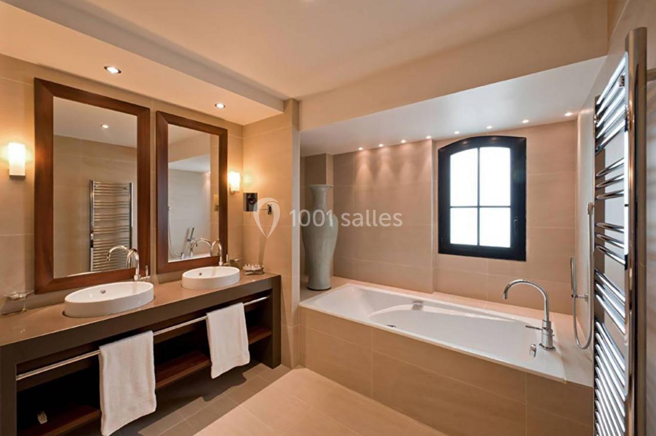 Salle de bain moderne avec double vasque, baignoire encastrée, miroir en bois et fenêtre en arche.