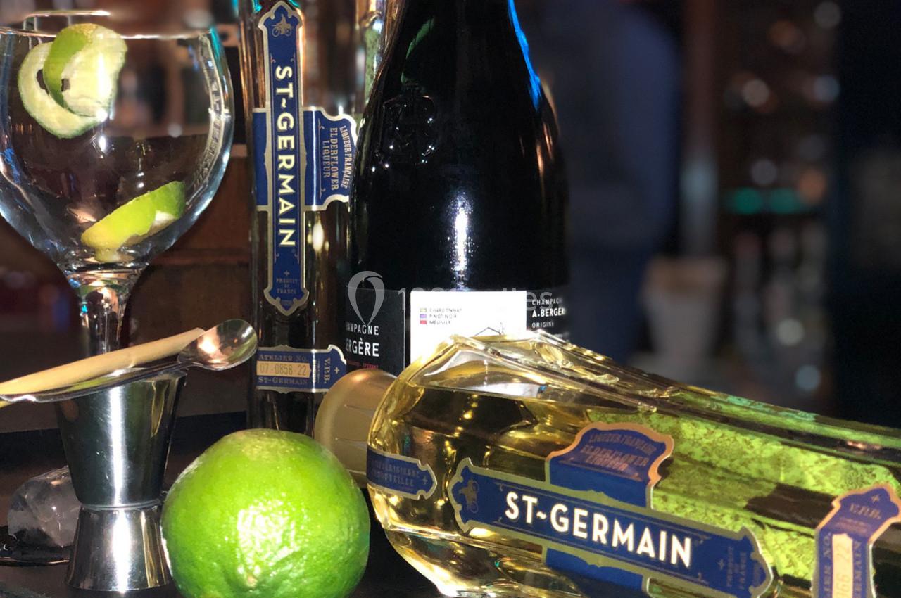 Verres, bouteille de liqueur St-Germain, lime et ustensiles de bar disposés sur un comptoir.