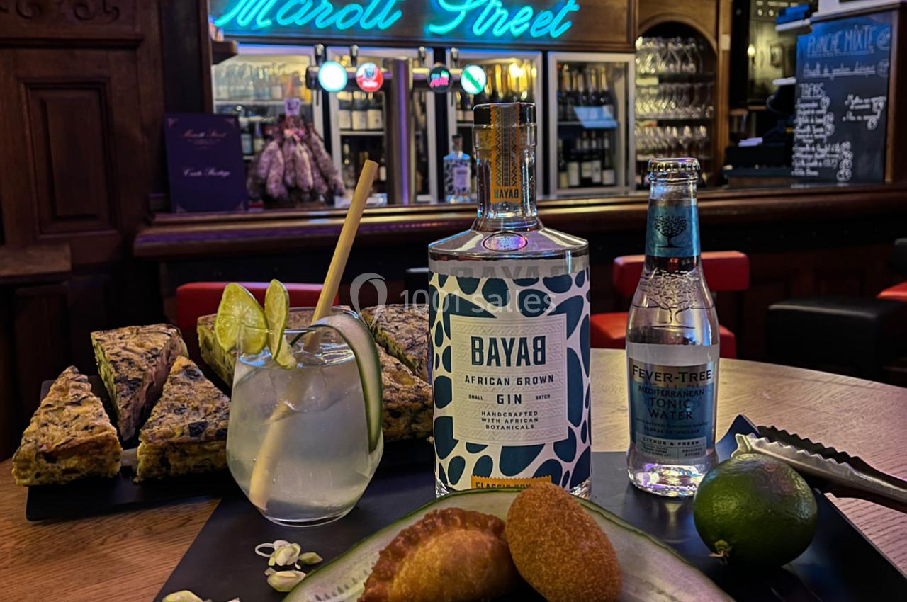 Un plateau avec gin, tonic, citron vert, empanadas et légumes, sur fond de bar avec enseigne lumineuse.