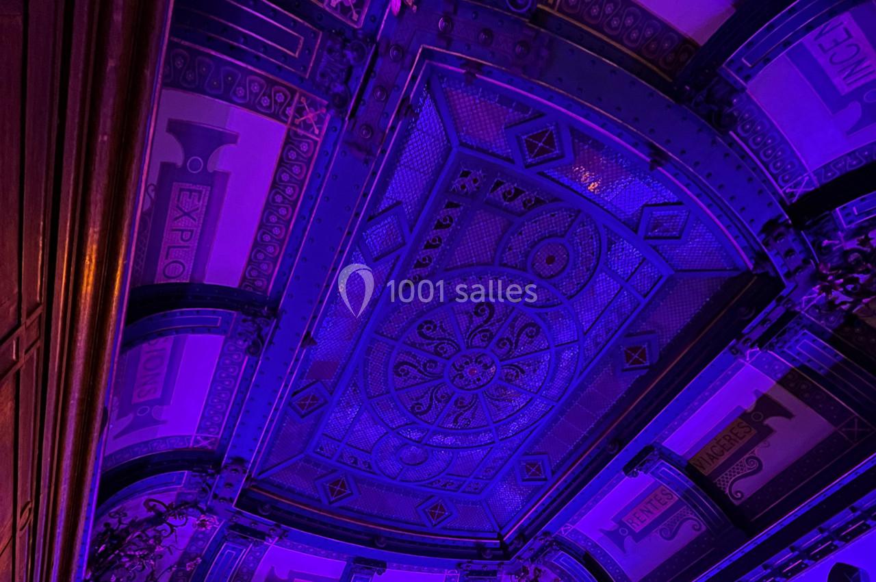 Plafond orné de motifs géométriques et éclairé par une lumière violette dans un intérieur richement décoré.