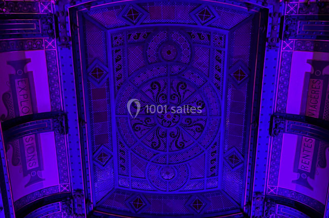 Plafond décoratif en métal orné de motifs géométriques et illuminé par une lumière violette.