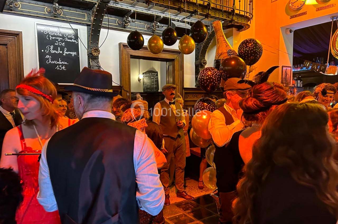 Groupe de personnes en tenue rétro dans un bar décoré de ballons noirs et dorés, ambiance festive et chaleureuse.