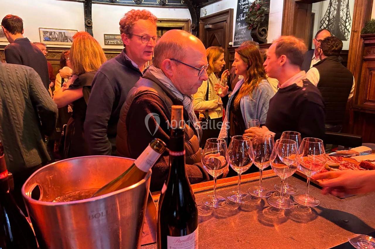Des personnes discutent et dégustent du vin dans un bar ou une salle conviviale, avec des bouteilles et des verres sur le…