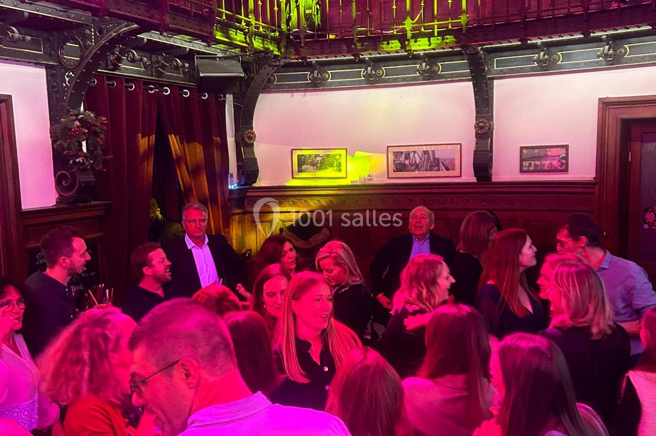Groupe de personnes discutant et partageant un moment convivial dans une salle à la décoration chaleureuse et boisée.