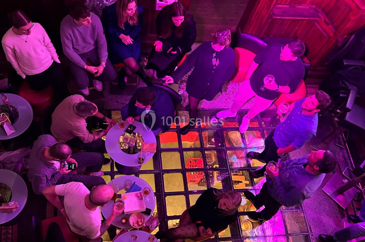 Groupe de personnes discutant autour de petites tables dans un espace intérieur éclairé par des lumières colorées.
