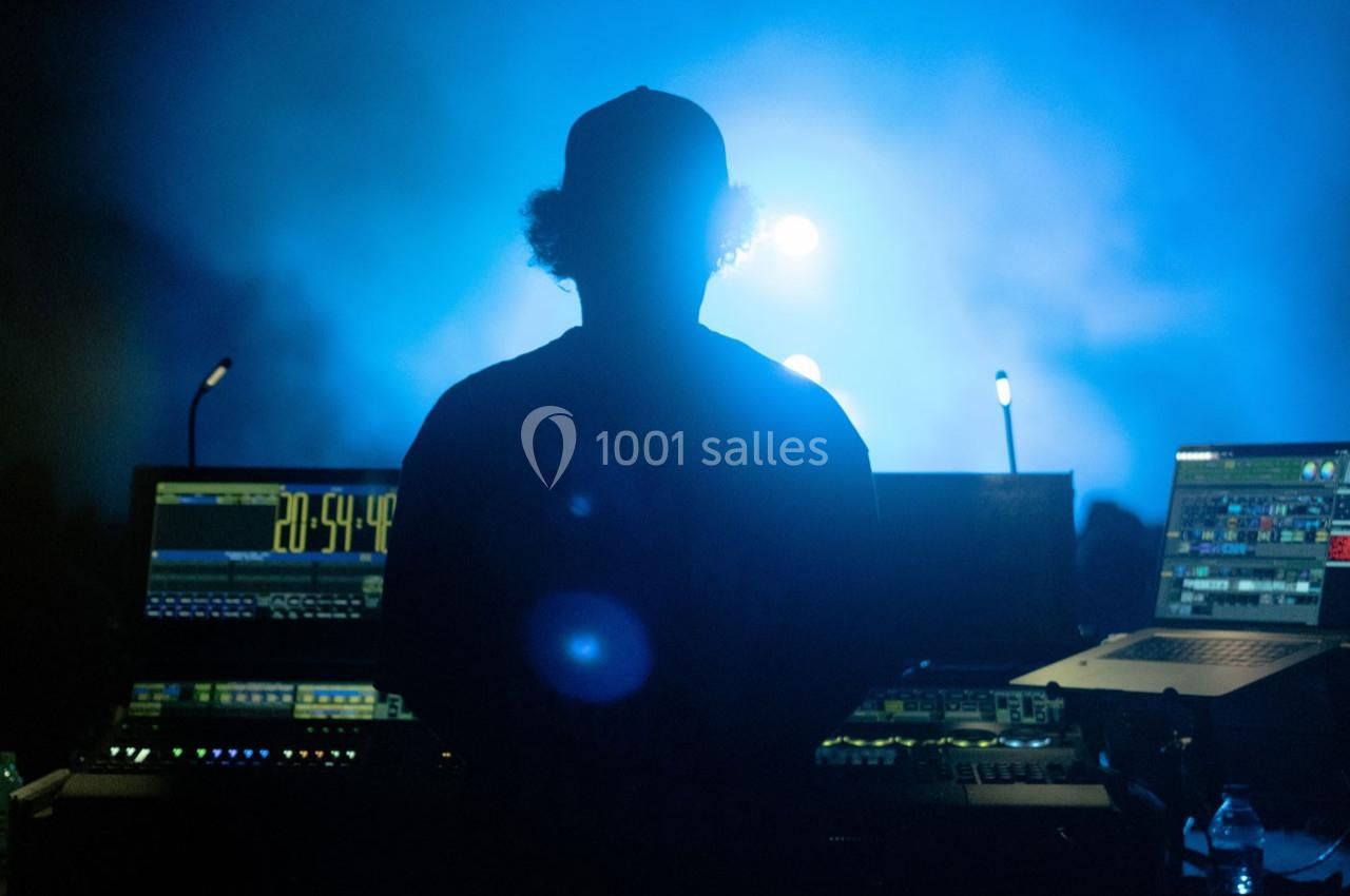 Technicien de dos devant une console de mixage éclairée, avec une lumière bleue diffuse en arrière-plan.