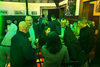 Groupe de personnes discutant dans un espace intérieur éclairé par des lumières vertes, ambiance conviviale.