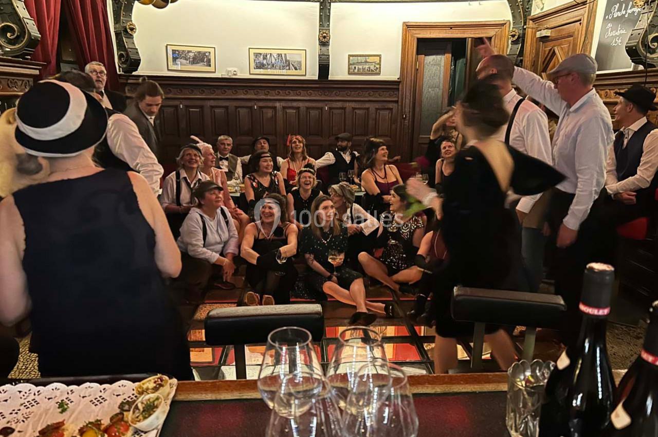 Groupe de personnes en tenue rétro rassemblées dans une salle décorée, avec des boissons et des amuse-gueules au premier…