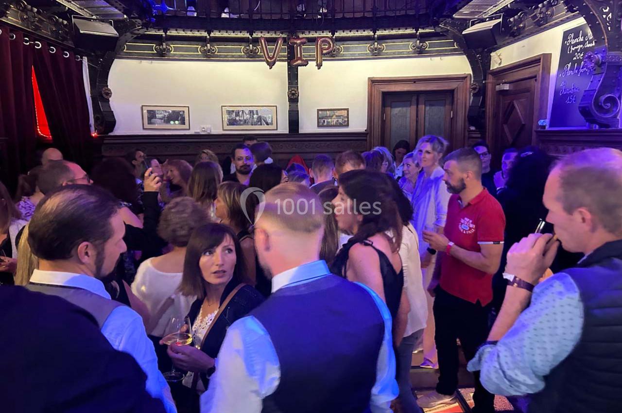Groupe de personnes discutant dans une salle élégante avec une ambiance tamisée et une pancarte ’VIP’ en arrière-plan.