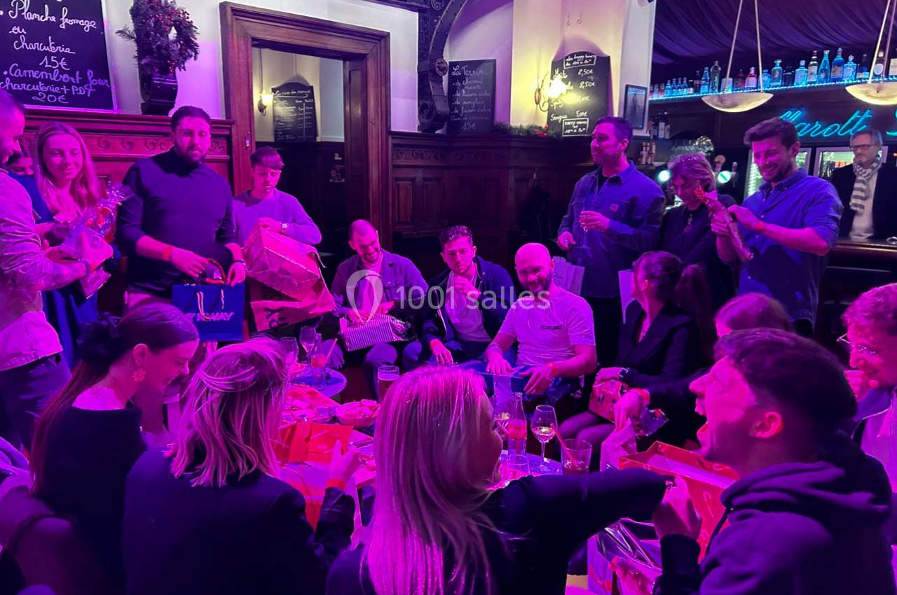 Un groupe de personnes assises et debout dans un bar, échangeant des cadeaux dans une ambiance conviviale.
