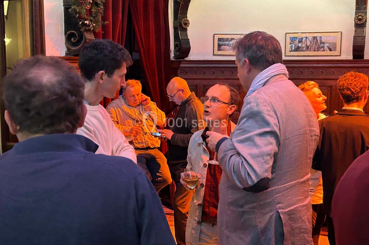 Groupe de personnes discutant dans un intérieur chaleureux avec des rideaux rouges et des cadres accrochés au mur.