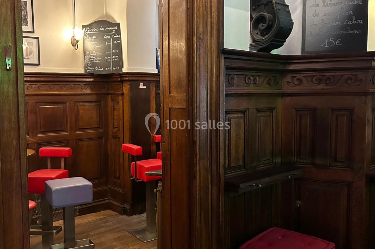 Intérieur d'un café avec boiseries, tabourets rouges et violets, et ardoises murales affichant des menus.