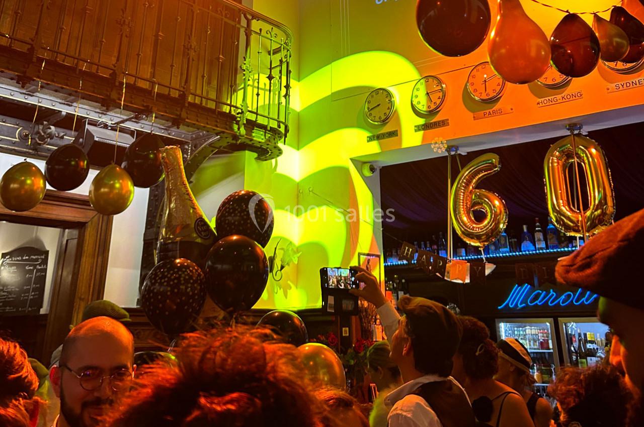 Fête animée avec des ballons dorés formant ’60’, des invités et une ambiance lumineuse chaleureuse.