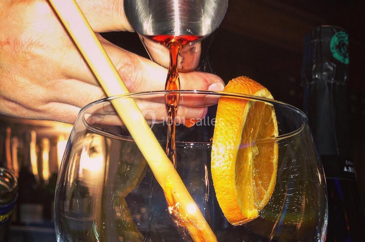 Un cocktail est préparé avec un liquide rouge versé dans un verre garni d'une tranche d'orange et d'une tige.