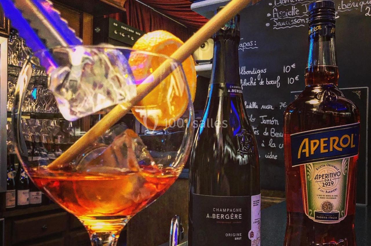 Verre de cocktail avec tranche d'orange, bouteille de champagne et Aperol sur un comptoir de bar.