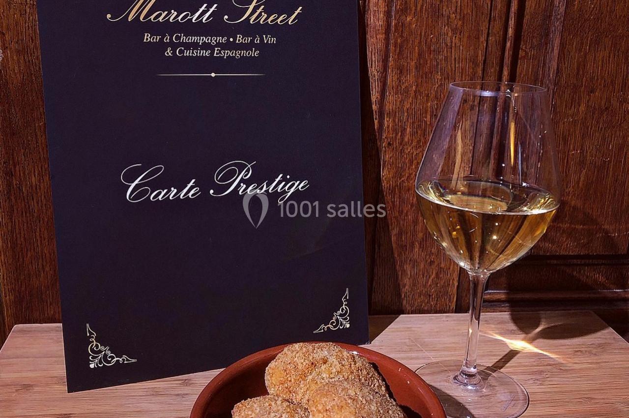 Carte de menu élégante posée sur une table en bois, accompagnée d'un verre de vin blanc et d'une assiette de tapas.