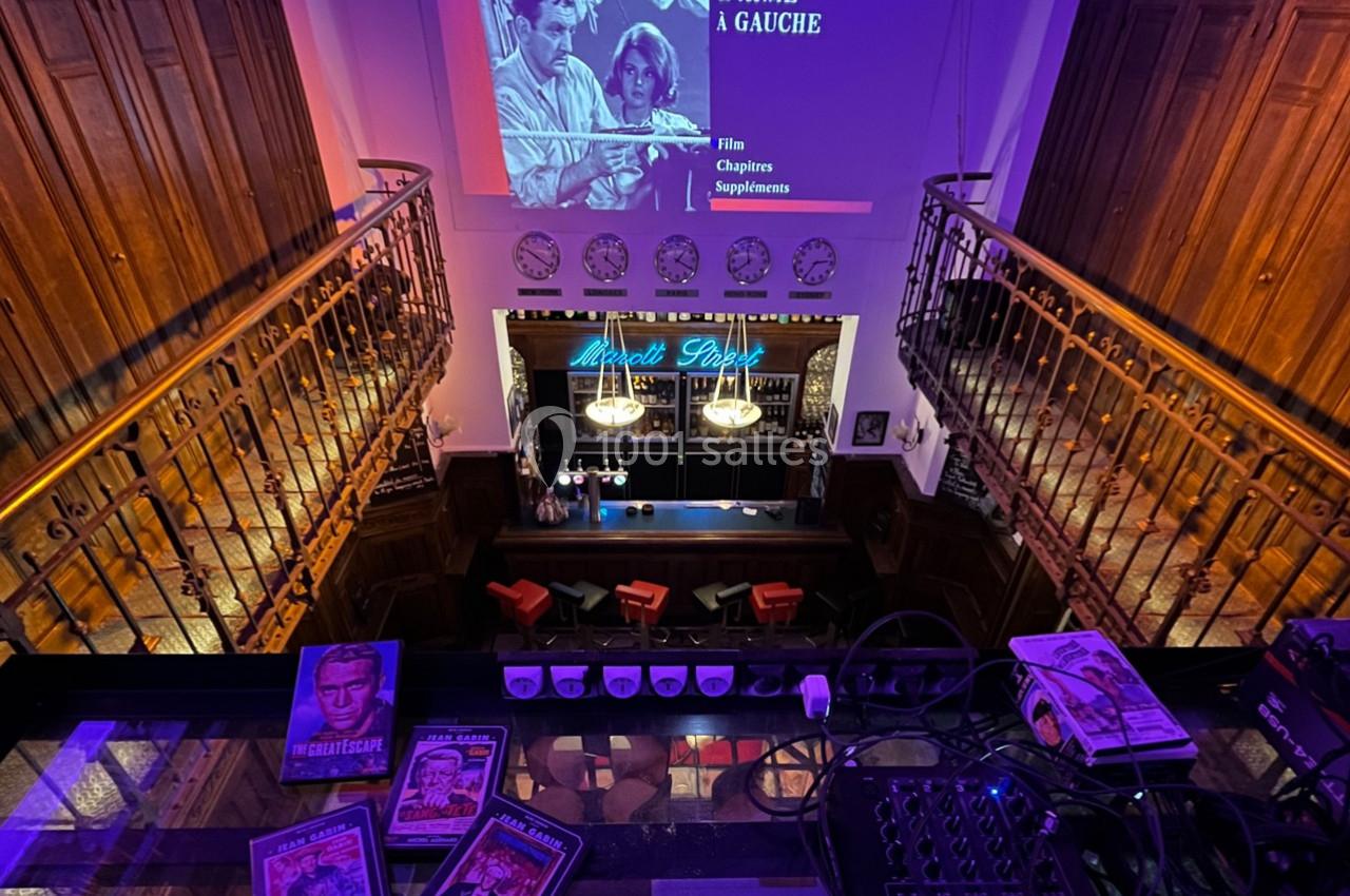 Vue plongeante sur un bar rétro avec une projection de film en arrière-plan et des magazines vintage au premier plan.