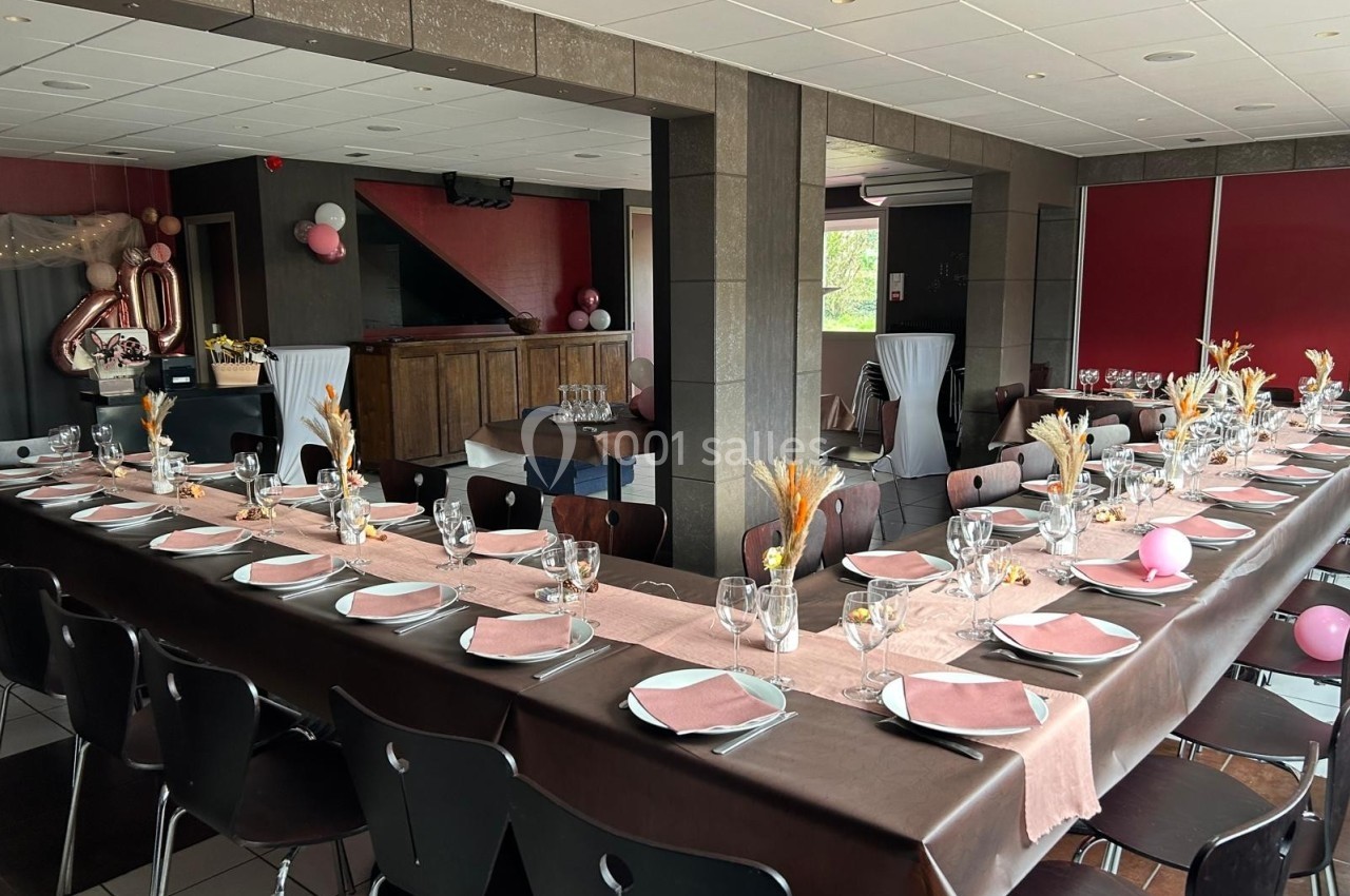 Salle décorée pour un événement avec tables en U dressées, nappes roses et marron, et décorations festives.