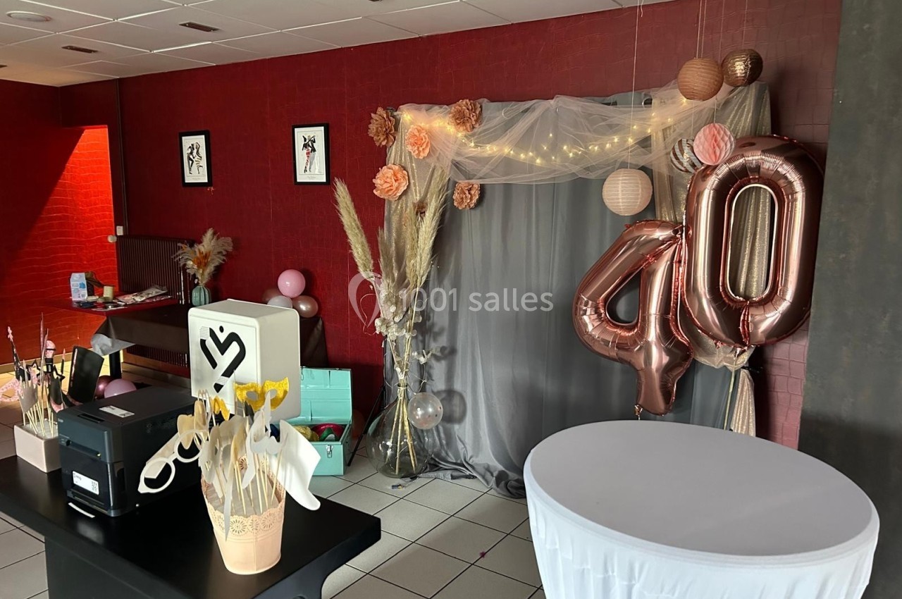 Décoration d'anniversaire avec ballons ’40’, rideau gris, fleurs séchées et guirlande lumineuse dans une salle.