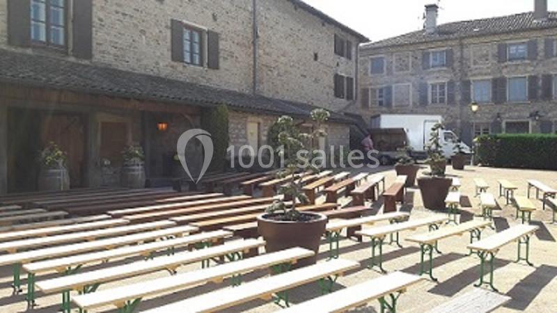 Bancs en bois alignés sur une place pavée devant des bâtiments en pierre, avec des plantes en pots.