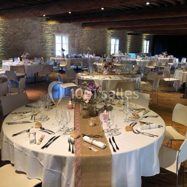 Salle de réception décorée avec des tables rondes dressées, nappes blanches et centre de table fleuri.