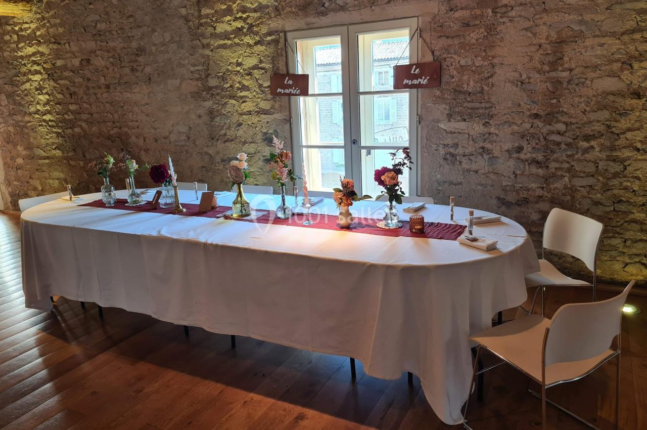 Table décorée avec nappes blanches, vases de fleurs et panneaux en bois, dans une salle aux murs en pierre.