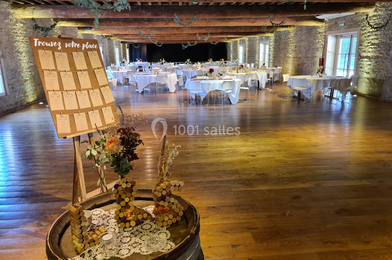 Salle de réception décorée avec des tables dressées et un plan de table sur chevalet en bois au premier plan.