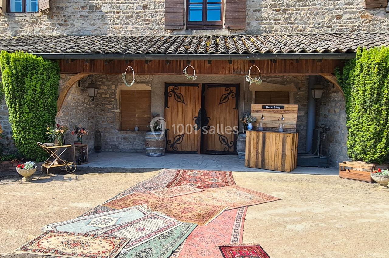 Entrée d'une maison en pierre avec porte en bois sculpté, tapis colorés au sol et décorations rustiques.