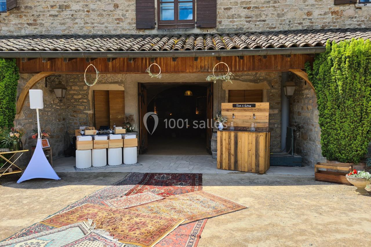 Entrée d'une grange en pierre avec tapis colorés au sol, bar en bois et décorations suspendues.