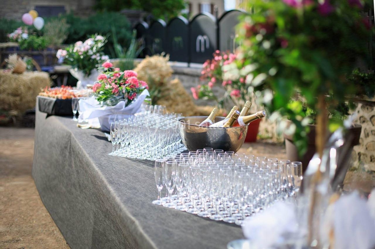 Table dressée en extérieur avec des verres, des bouteilles de champagne dans un seau et des décorations florales.
