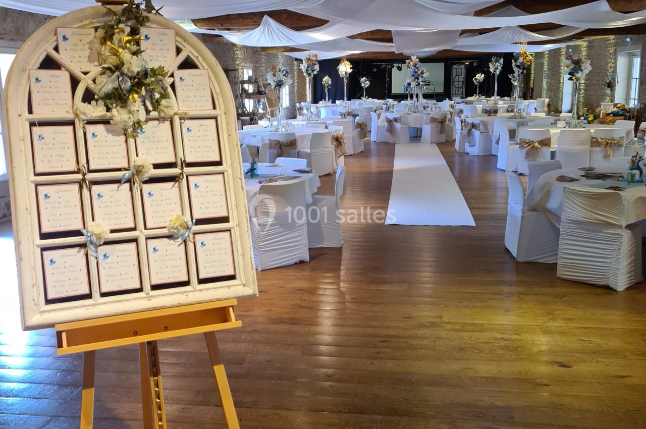 Salle de réception décorée pour un mariage avec un plan de table sur chevalet au premier plan.