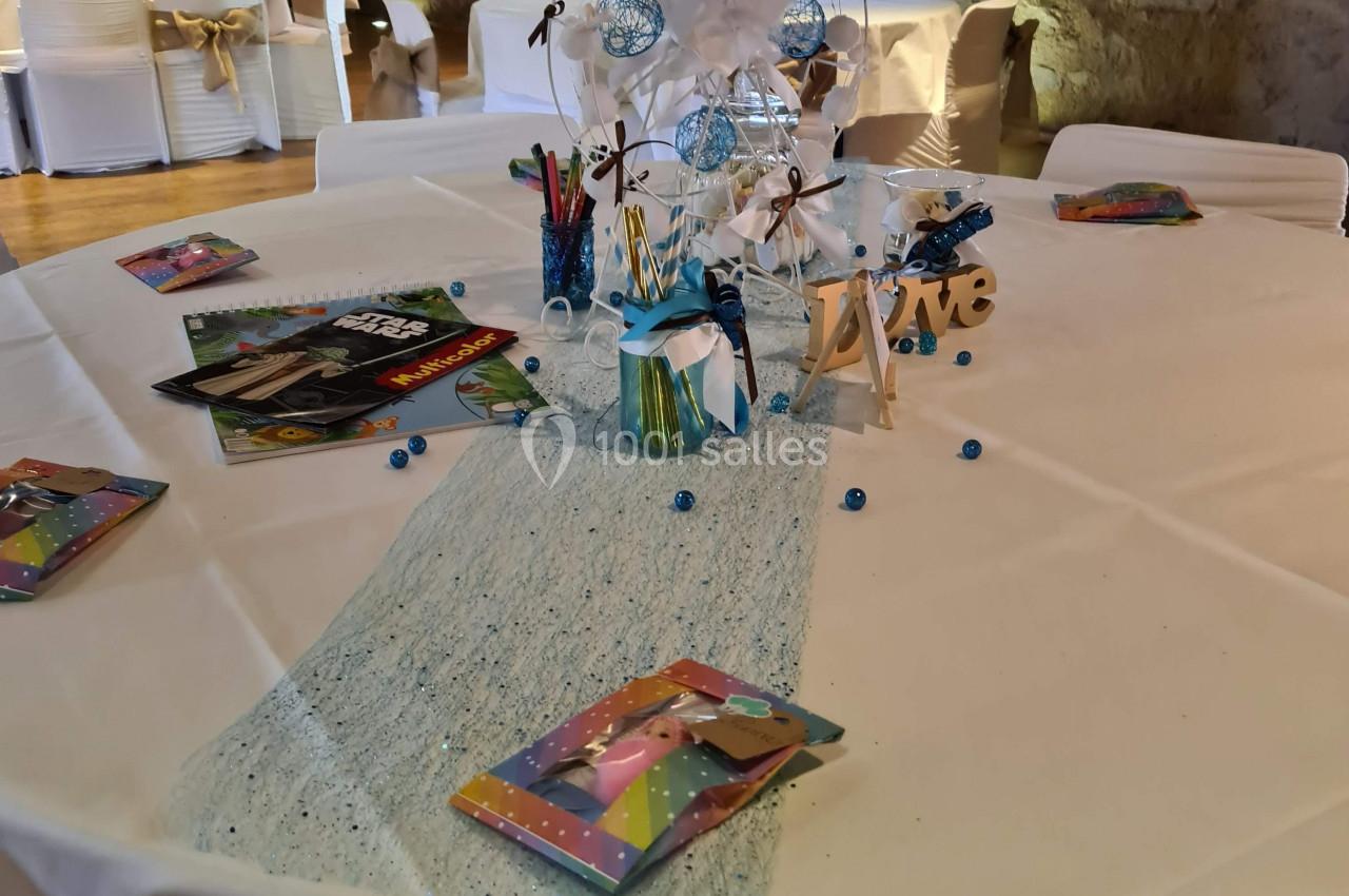 Table décorée pour un événement, avec nappe blanche, centre de table bleu et blanc, crayons et livrets colorés.