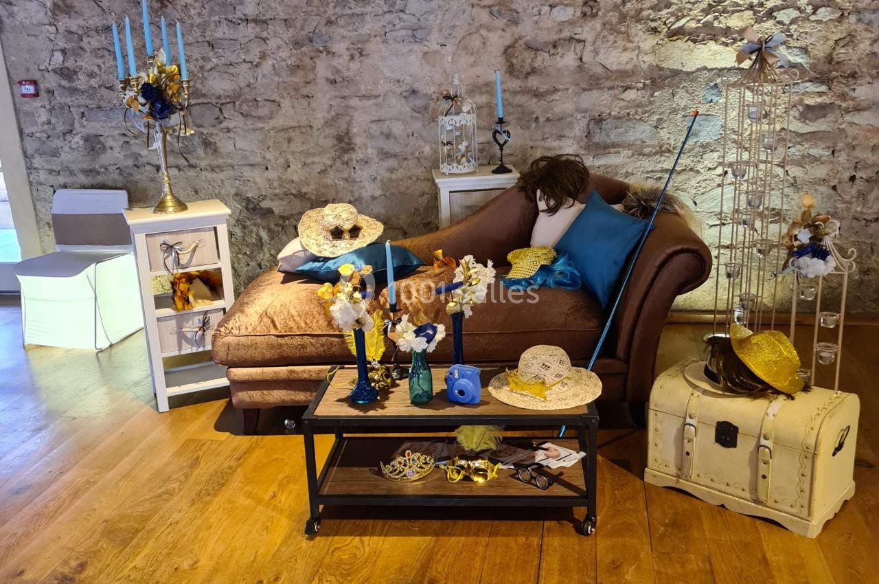 Salon décoré avec des objets vintage, des fleurs jaunes et bleues, sur un parquet en bois et un mur en pierre apparente.