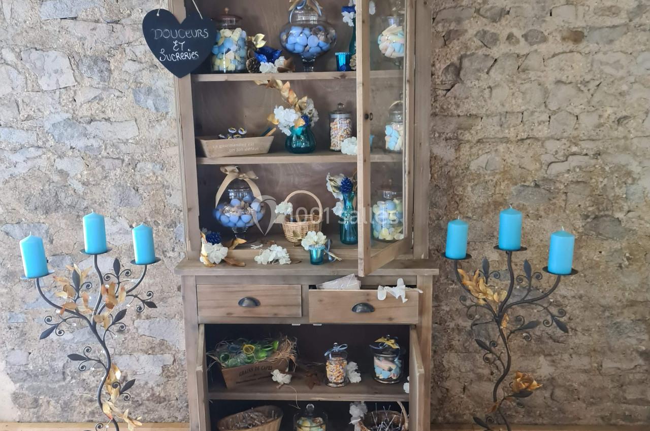 Vaisselier en bois rempli de pots et décorations, entouré de chandeliers avec bougies bleues, sur un sol en bois.