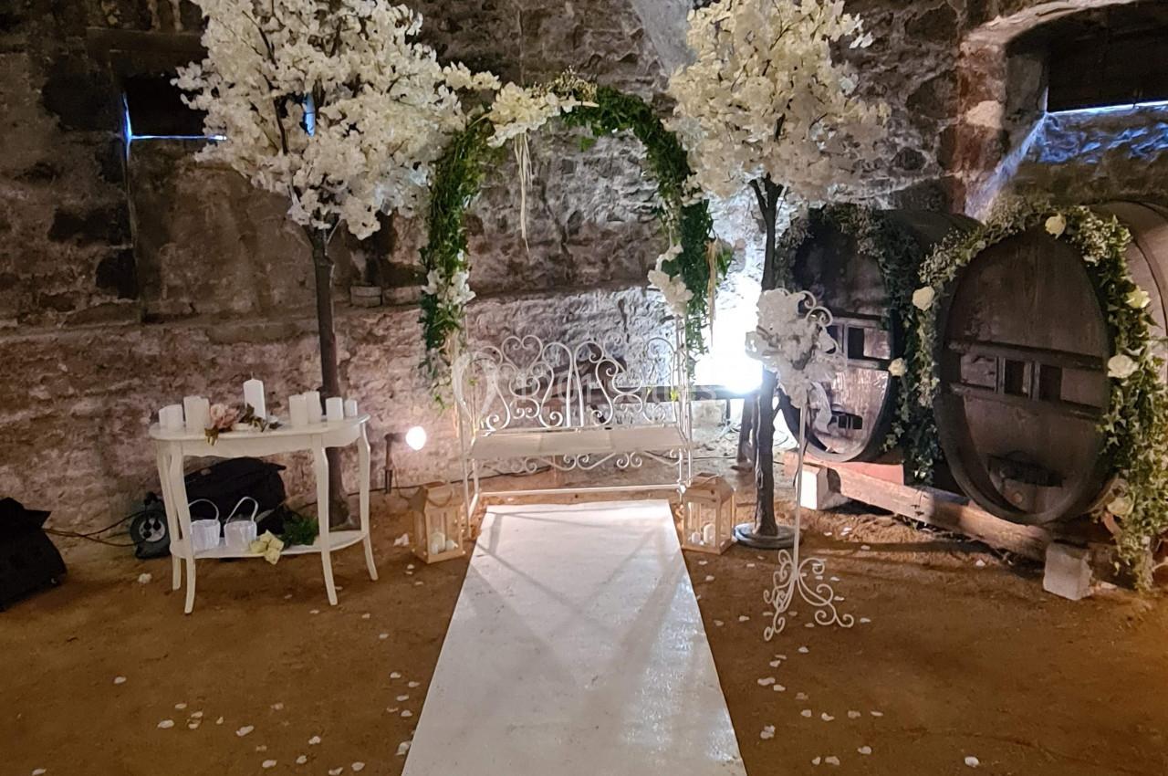 Allée blanche menant à une arche décorée de fleurs blanches et vertes dans une cave voûtée en pierre.