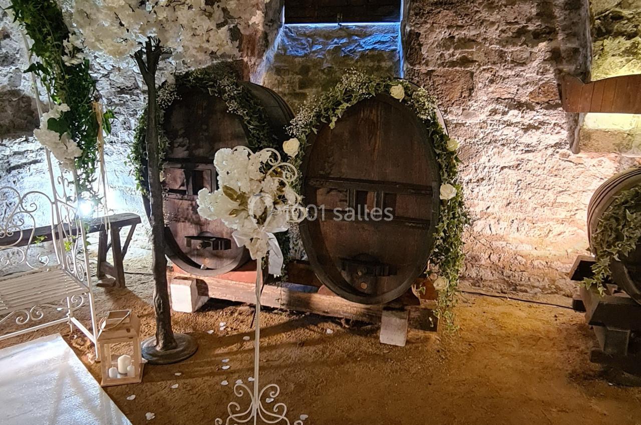 Deux tonneaux en bois décorés de fleurs blanches et de verdure dans une cave voûtée en pierre.