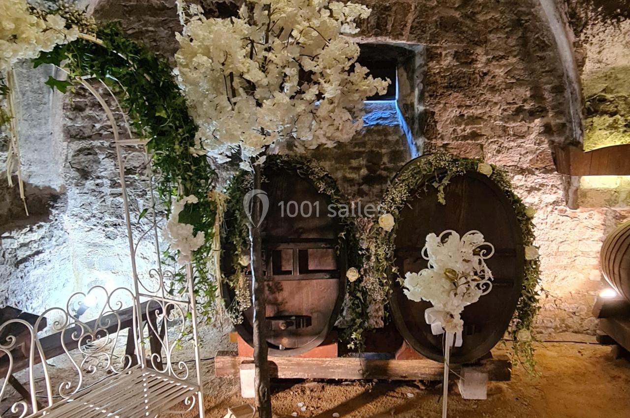 Décoration florale blanche avec tonneaux en bois et arche dans une cave voûtée en pierre.