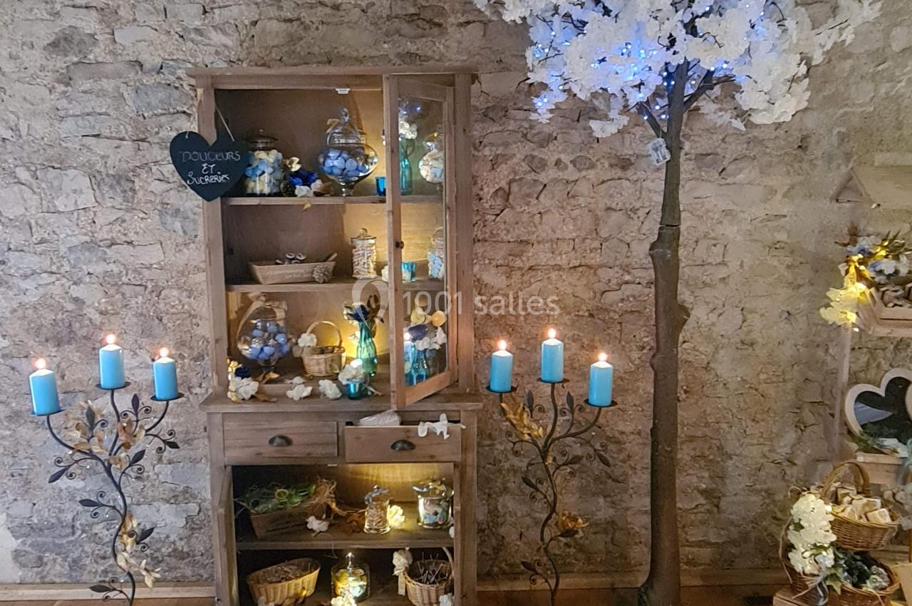 Meuble en bois décoré de bougies et d'objets, avec un arbre artificiel illuminé dans une pièce aux murs en pierre.