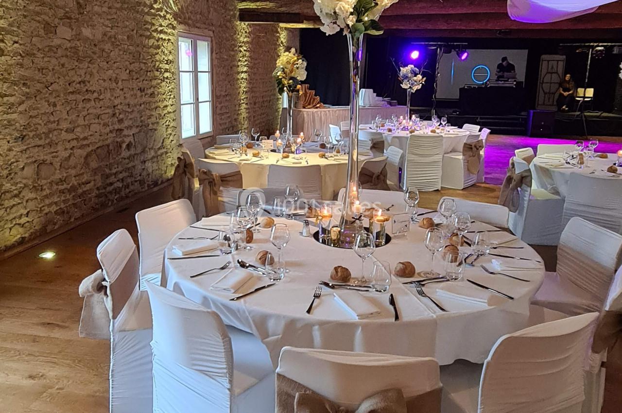 Salle de réception décorée avec des tables rondes, nappes blanches, chaises ornées de nœuds et centre de table floral.