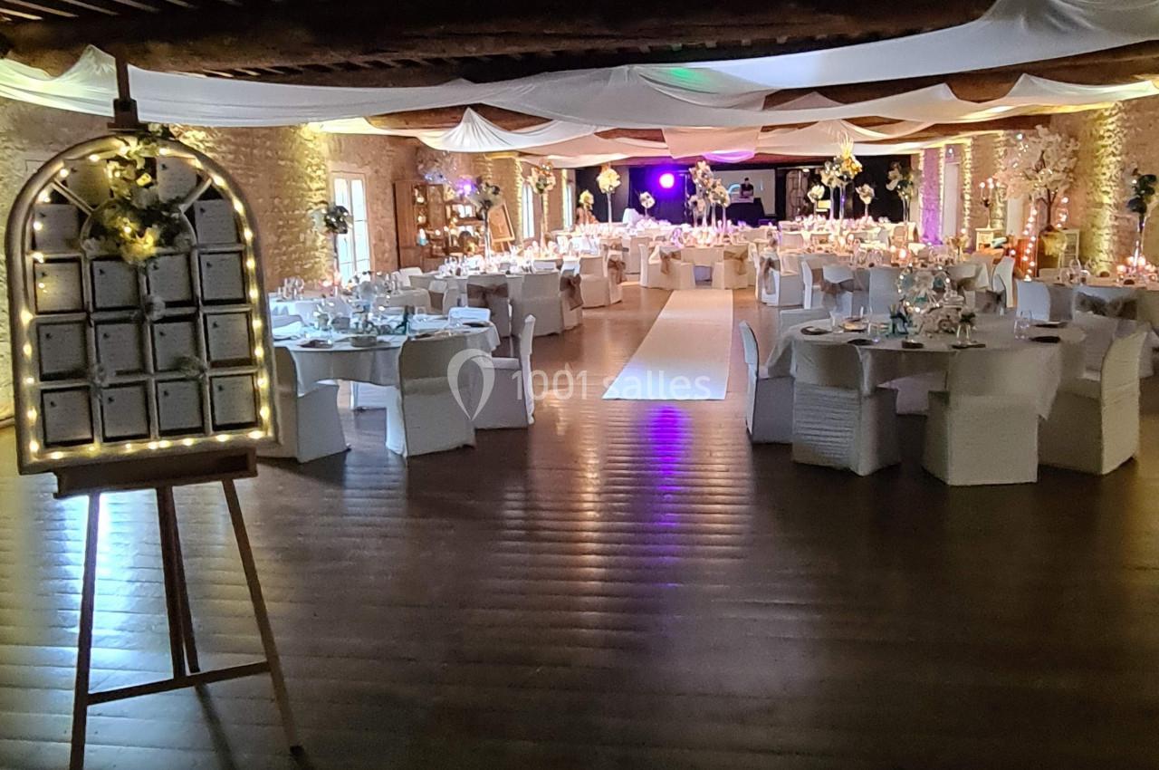 Salle de réception décorée pour un événement, avec tables dressées, éclairages chaleureux et allée centrale.
