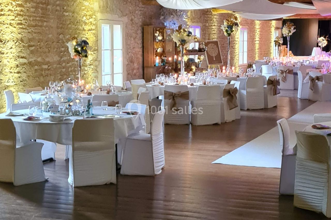 Salle de réception décorée avec des tables rondes, nappes blanches, chaises habillées et éclairage chaleureux.