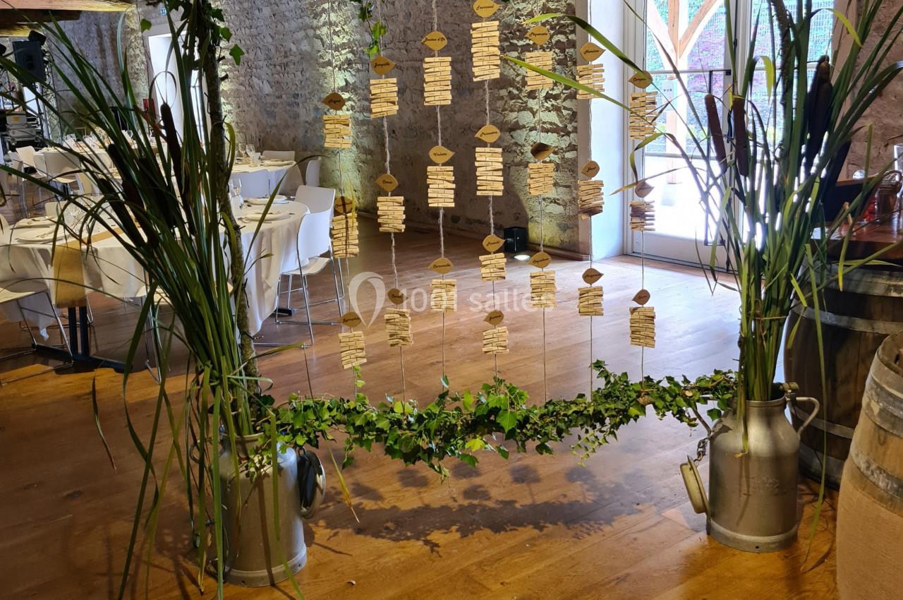 Cadre décoratif en bois et feuillage suspendant des étiquettes, installé dans une salle de réception rustique.