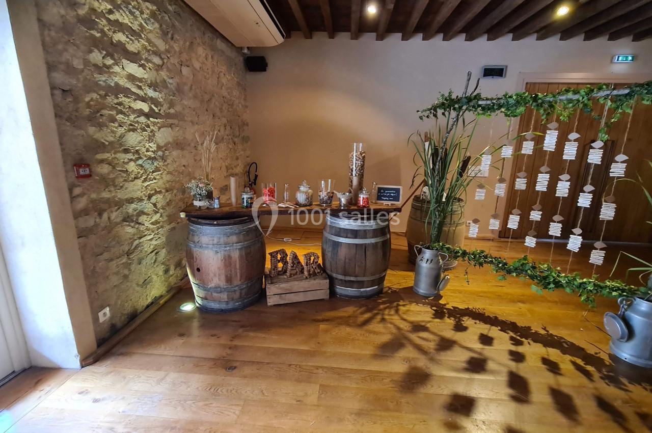 Deux tonneaux en bois formant un bar décoré, entourés de plantes et d'éléments rustiques dans une salle en pierre.