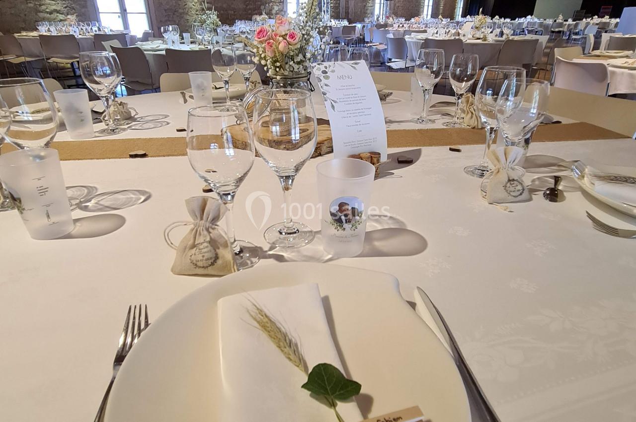 Table dressée pour un repas, avec assiette, serviette décorée, couverts, verres et centre de table floral dans une salle en…