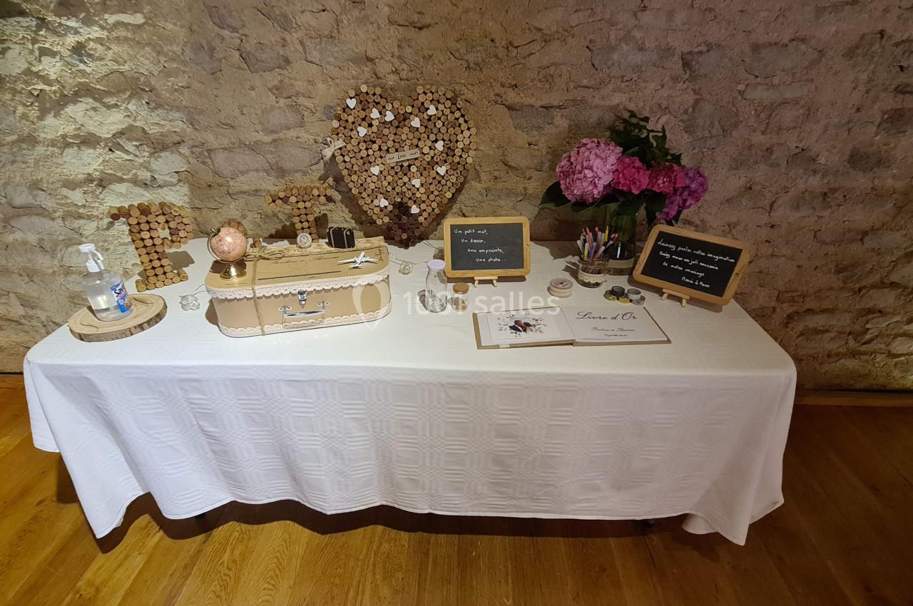 Table décorée pour un mariage avec urne, panneaux en ardoise, fleurs roses et mur en pierre en arrière-plan.