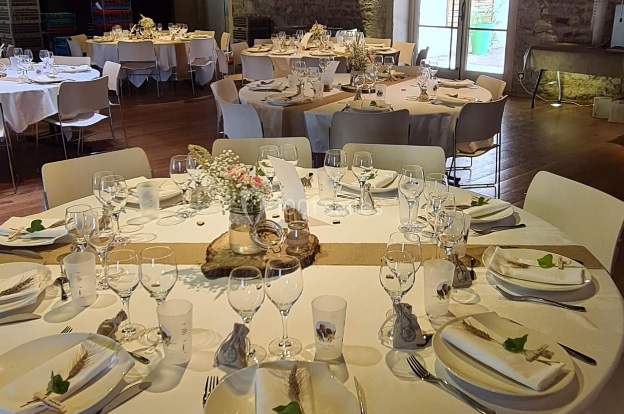 Salle de réception avec tables rondes dressées, nappes blanches, vaisselle élégante et décoration florale.